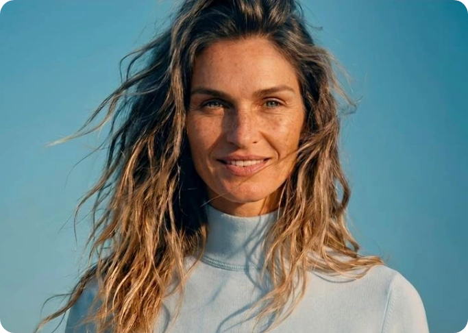 Portrait of a smiling woman with wind-swept hair against a clear blue sky.